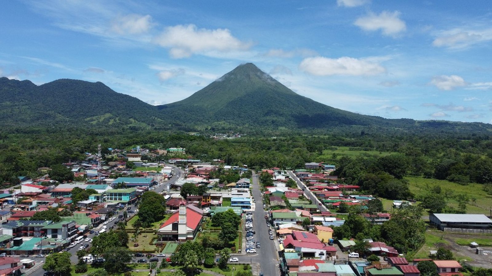 Vista aérea del pueblo de La Fortuna con techos coloridos y el Volcán Arenal al fondo bajo un cielo parcialmente nublado